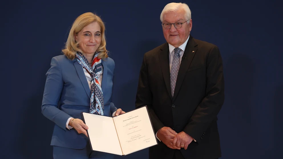 Nina Warken standing with Federal President Frank-Walter Steinmeier and holding a certificate, in front of a dark blue backdrop