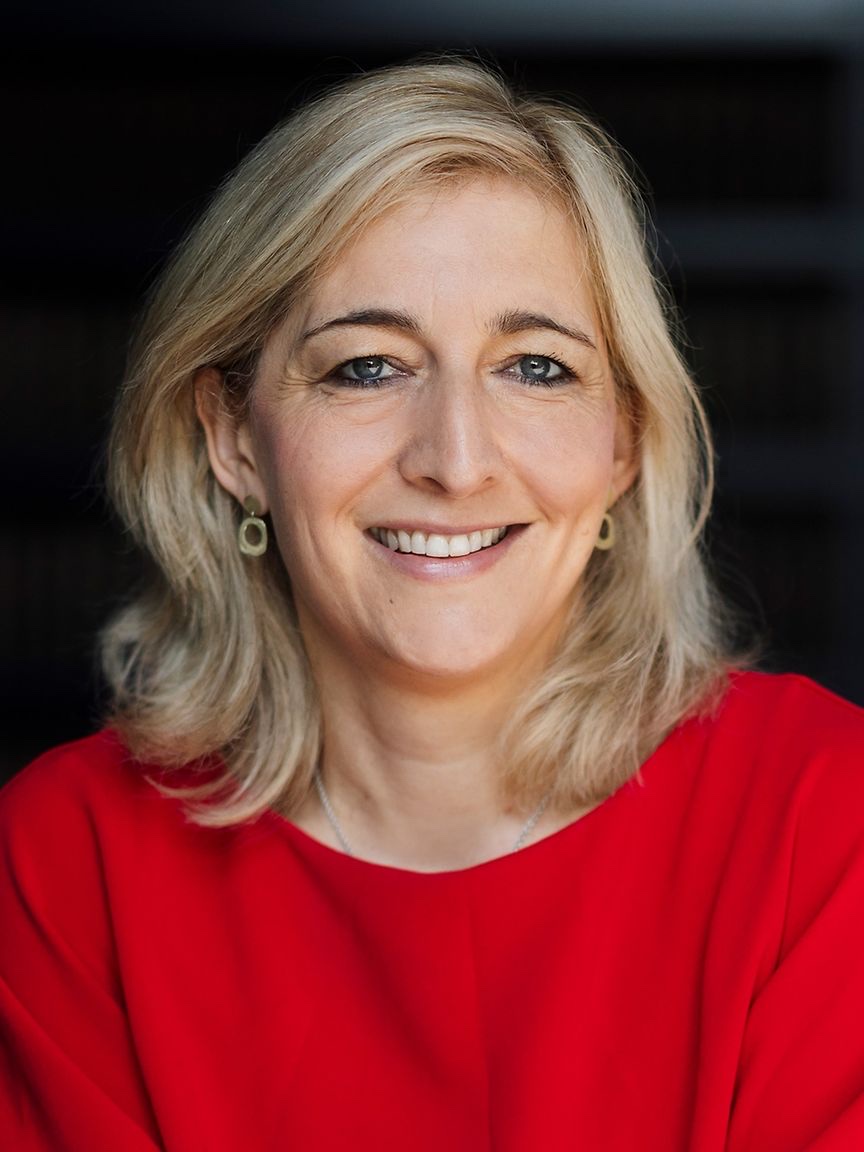 Nina Warken, head-and-shoulders portrait in a red top against a dark background