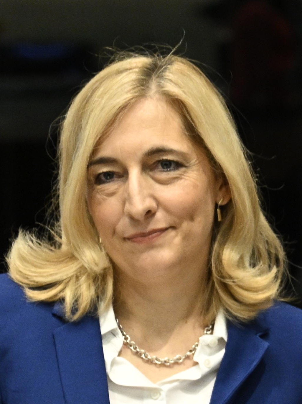 Head-and-shoulders portrait of Nina Warken, smiling, in a blue blazer and white blouse against a dark background