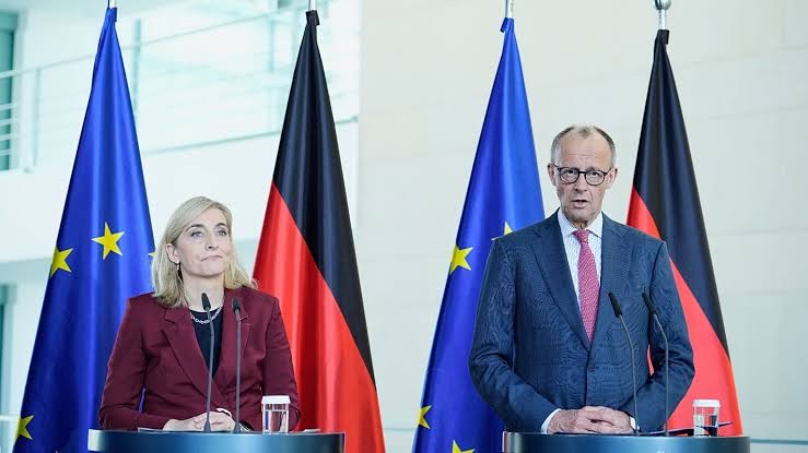 Nina Warken and Chancellor Friedrich Merz at two lecterns in a bright hall, with alternating German and European flags behind them