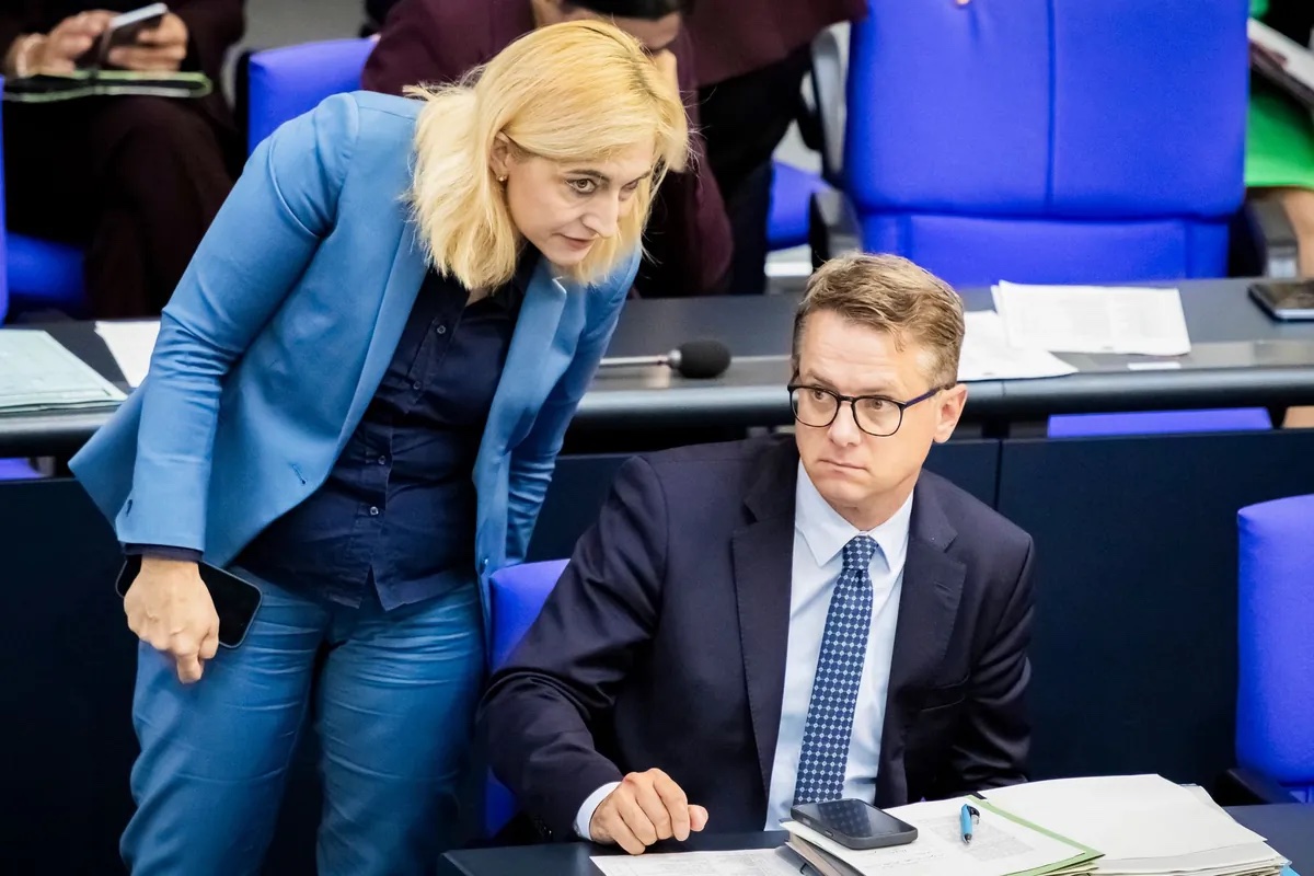 Nina Warken leaning over the government bench in the Bundestag to speak with a colleague