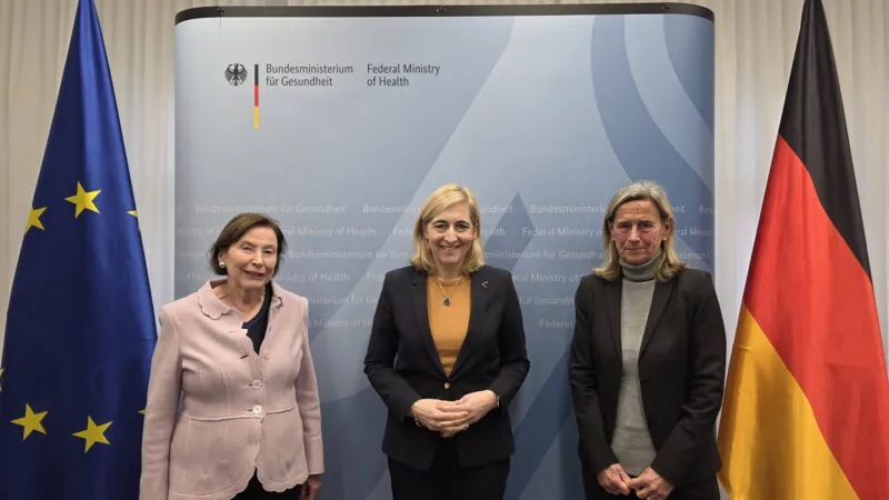 Nina Warken with two other women standing in front of a Federal Ministry of Health backdrop, with German and EU flags