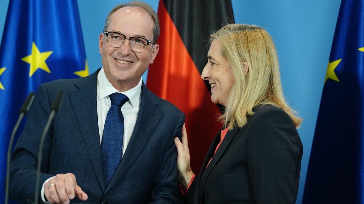 Nina Warken standing beside a male politician at a press appearance, with flags in the background